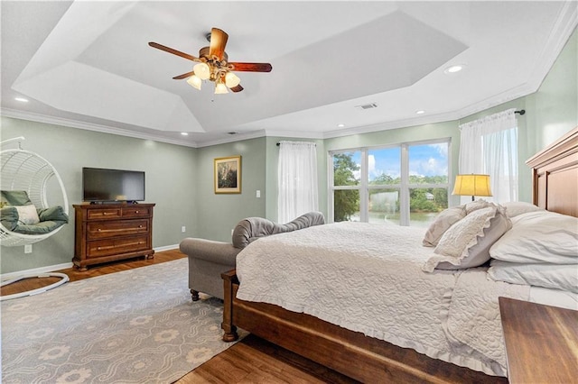 bedroom with baseboards, visible vents, wood finished floors, a tray ceiling, and crown molding