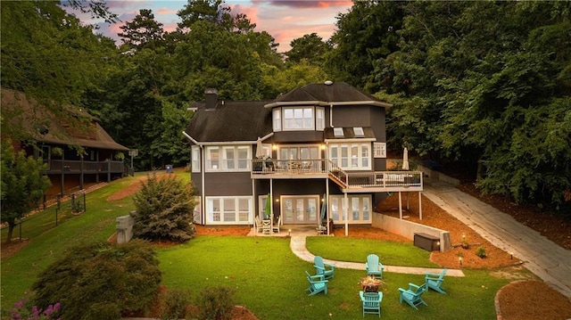 back of property at dusk featuring a deck, fence, a yard, french doors, and a chimney