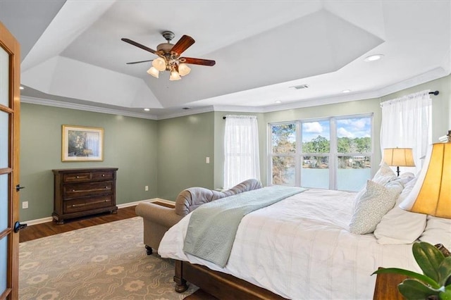 bedroom featuring wood finished floors, a ceiling fan, baseboards, a raised ceiling, and crown molding