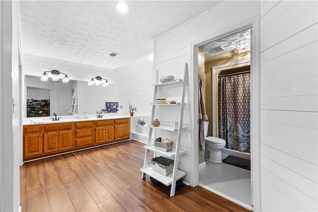 full bath with double vanity, visible vents, a sink, a textured ceiling, and wood finished floors