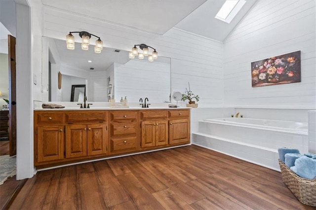 full bath with double vanity, a sink, wood finished floors, vaulted ceiling with skylight, and a bath