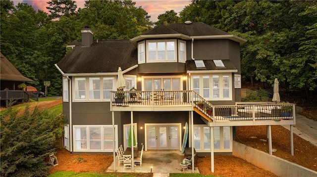 rear view of house featuring french doors, a patio, a chimney, stucco siding, and a deck