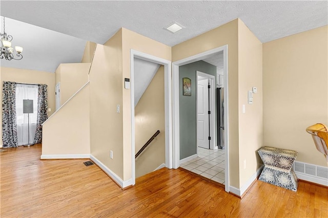 corridor featuring light wood-style floors, visible vents, a notable chandelier, and an upstairs landing