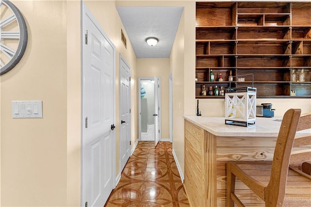 hall featuring visible vents, a textured ceiling, and baseboards