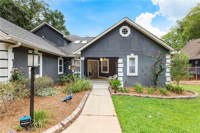 view of front facade with roof with shingles, a front yard, a porch, and stucco siding