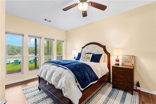 bedroom with a ceiling fan, visible vents, baseboards, and wood finished floors