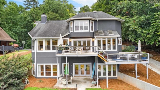 rear view of house with a deck, french doors, stucco siding, a chimney, and a patio area