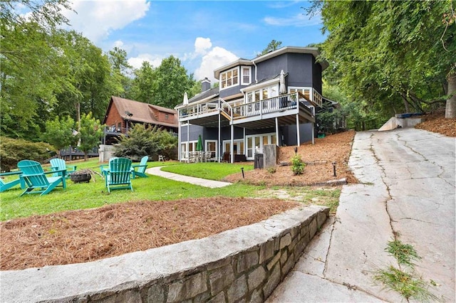 rear view of property featuring an outdoor fire pit, a lawn, a wooden deck, and stucco siding