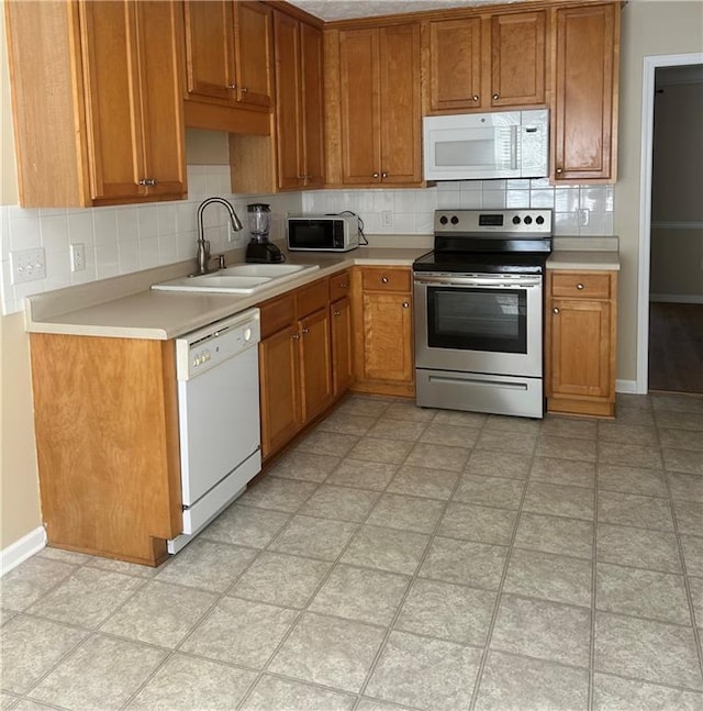 kitchen with tasteful backsplash, light countertops, brown cabinetry, a sink, and white appliances