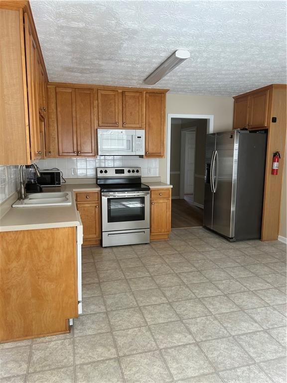 kitchen with a sink, light countertops, appliances with stainless steel finishes, backsplash, and brown cabinets