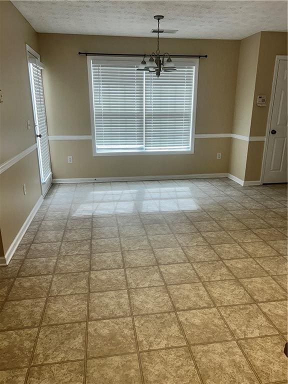 unfurnished dining area with visible vents, a notable chandelier, a textured ceiling, and baseboards