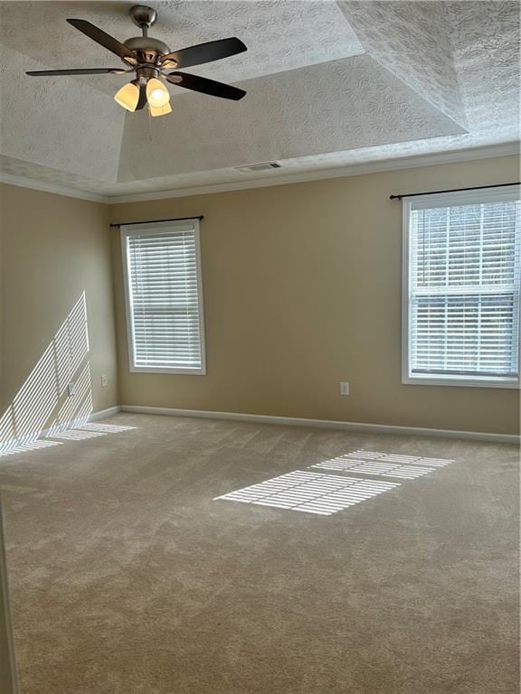 carpeted spare room with a textured ceiling, a tray ceiling, ornamental molding, and baseboards