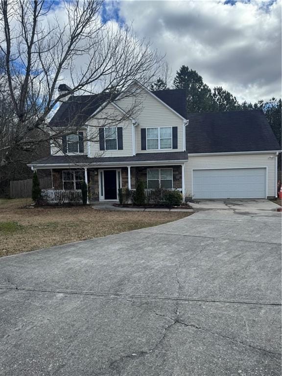 traditional home featuring driveway, covered porch, an attached garage, and fence