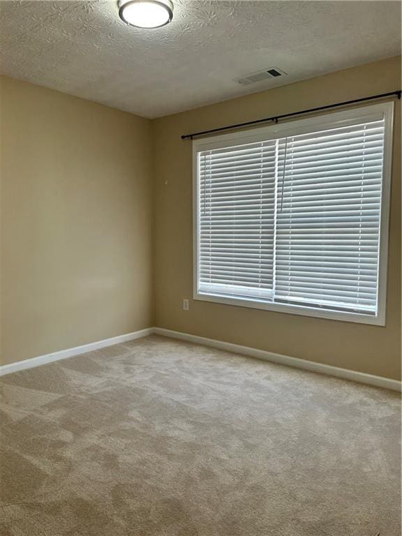 spare room featuring carpet floors, visible vents, a textured ceiling, and baseboards