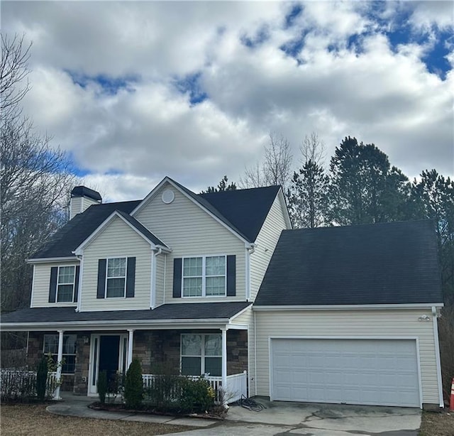 traditional-style home with covered porch, a garage, stone siding, concrete driveway, and a chimney