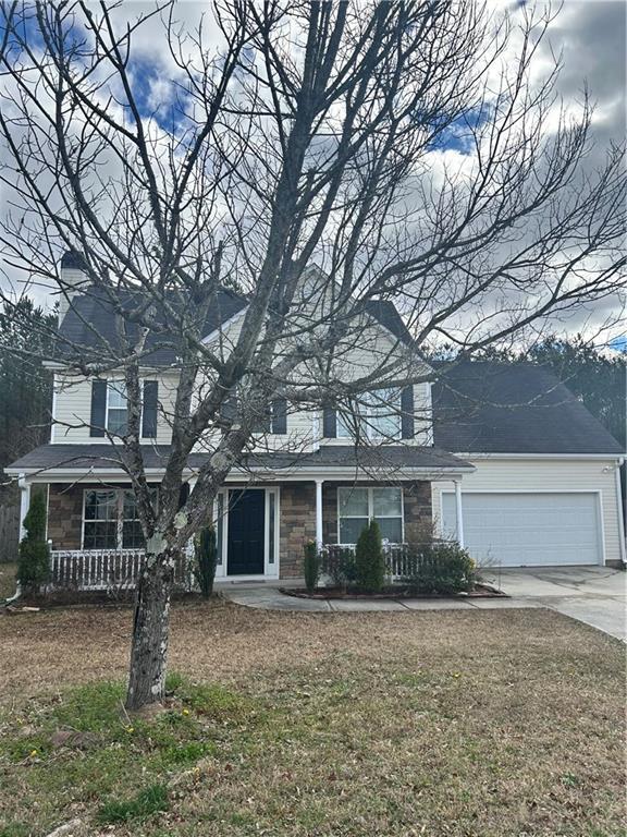 traditional-style home featuring a porch, concrete driveway, an attached garage, stone siding, and a front lawn