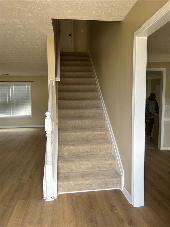 staircase featuring a textured ceiling, baseboards, and wood finished floors