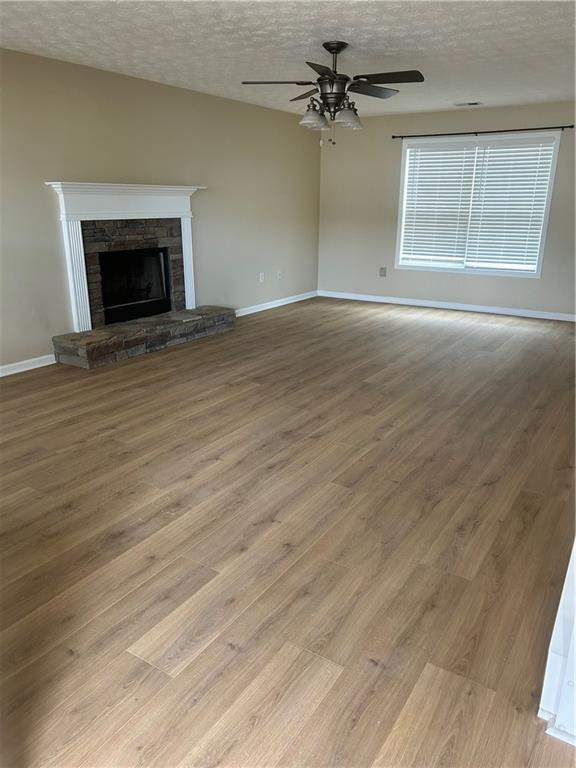 unfurnished living room featuring a ceiling fan, a fireplace, a textured ceiling, and wood finished floors