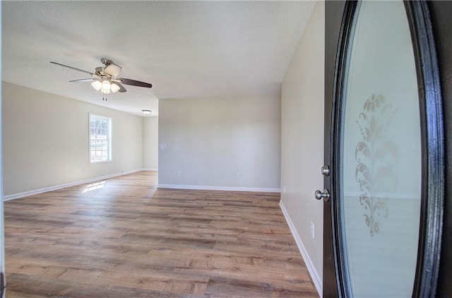 spare room with a ceiling fan, wood finished floors, baseboards, and a textured ceiling