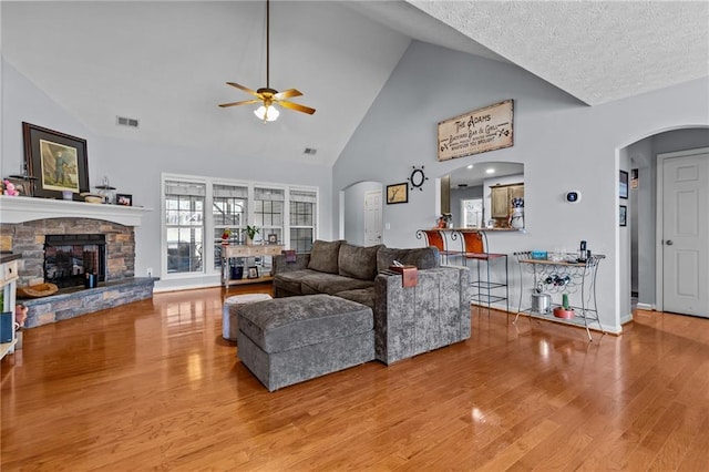 living room featuring ceiling fan, a stone fireplace, high vaulted ceiling, and light wood-type flooring