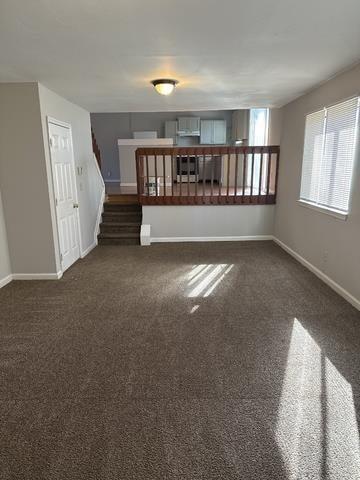 unfurnished living room featuring stairway, carpet flooring, and baseboards