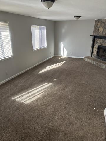 unfurnished living room with dark colored carpet, plenty of natural light, and baseboards