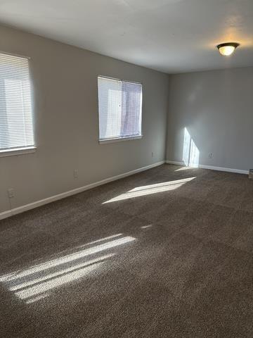 unfurnished room featuring dark carpet and baseboards