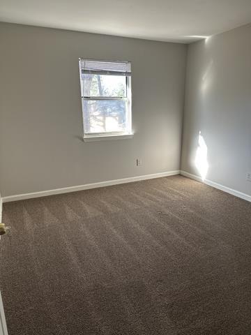empty room featuring baseboards and dark carpet