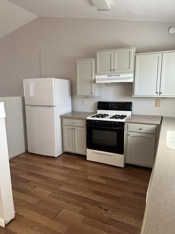 kitchen featuring white appliances, under cabinet range hood, vaulted ceiling, light countertops, and wood finished floors