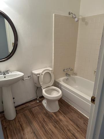 full bath with wood finished floors, shower / bathtub combination, toilet, and a sink