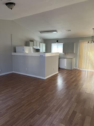 unfurnished living room featuring dark wood-style flooring, baseboards, a chandelier, and vaulted ceiling