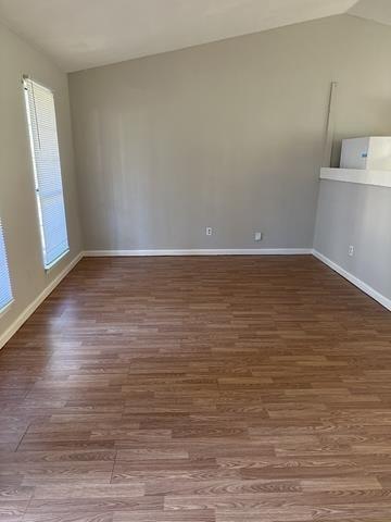 empty room featuring wood finished floors, baseboards, and lofted ceiling