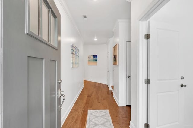 corridor with ornamental molding and light hardwood / wood-style flooring