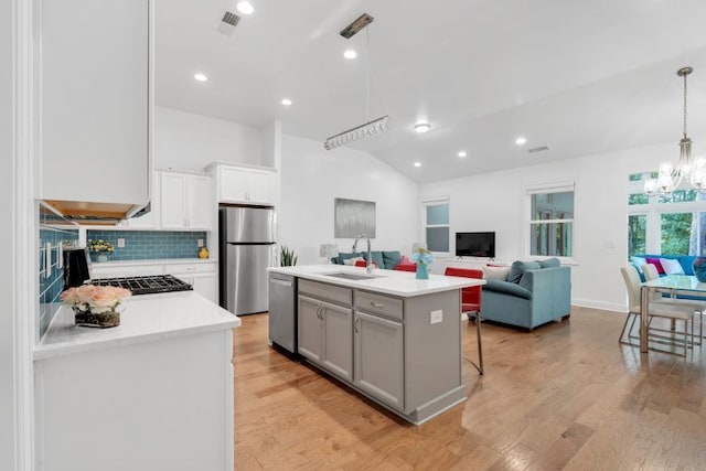 kitchen with backsplash, light hardwood / wood-style floors, appliances with stainless steel finishes, sink, and a center island with sink