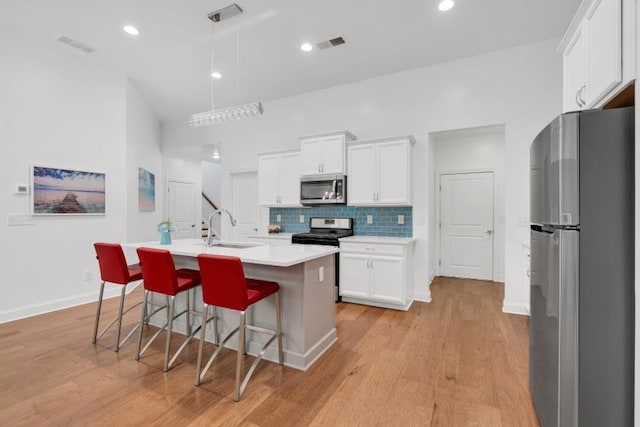 kitchen with appliances with stainless steel finishes, a center island with sink, sink, decorative backsplash, and light wood-type flooring