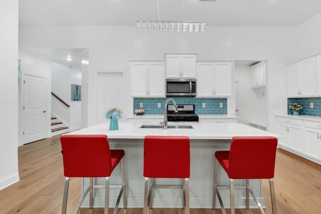 kitchen with light hardwood / wood-style floors, a kitchen island with sink, decorative backsplash, and stainless steel appliances