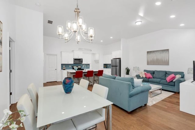 dining room with an inviting chandelier, light hardwood / wood-style flooring, and lofted ceiling