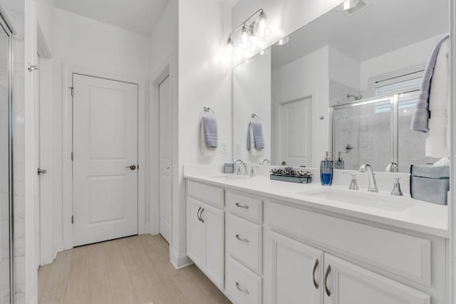 bathroom featuring dual vanity, a shower with shower door, and hardwood / wood-style floors