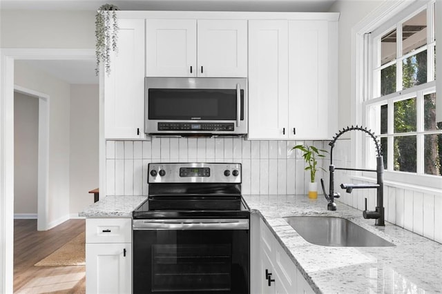 kitchen with light stone countertops, appliances with stainless steel finishes, white cabinetry, and sink