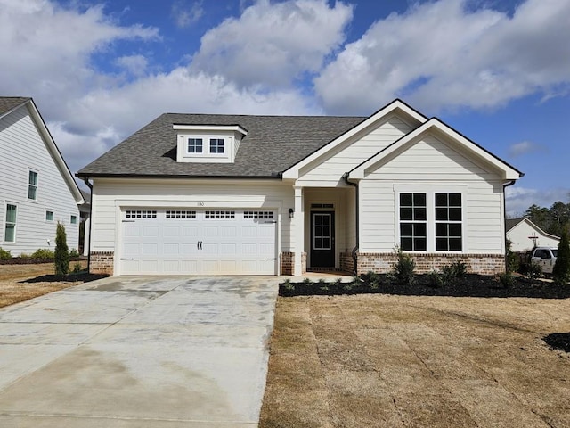 craftsman house featuring concrete driveway, brick siding, an attached garage, and a shingled roof