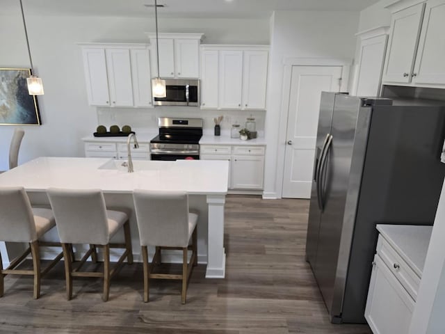 kitchen featuring hanging light fixtures, stainless steel appliances, a kitchen breakfast bar, dark hardwood / wood-style flooring, and white cabinets