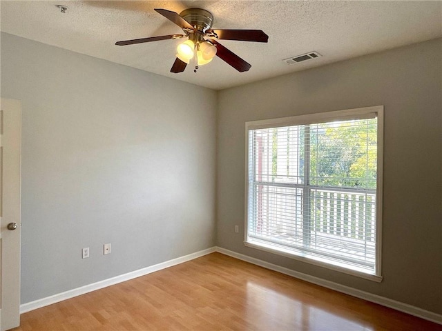 unfurnished room with ceiling fan, a wealth of natural light, a textured ceiling, and light wood-type flooring