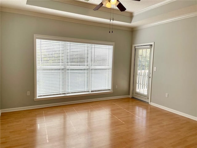 empty room featuring a raised ceiling, crown molding, ceiling fan, and light hardwood / wood-style floors