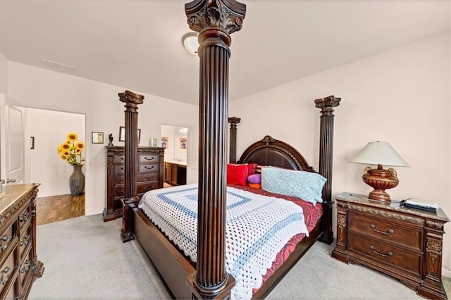 bedroom featuring ensuite bathroom, light colored carpet, and decorative columns