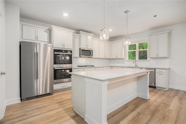 kitchen featuring a center island, hanging light fixtures, stainless steel appliances, white cabinets, and light hardwood / wood-style flooring