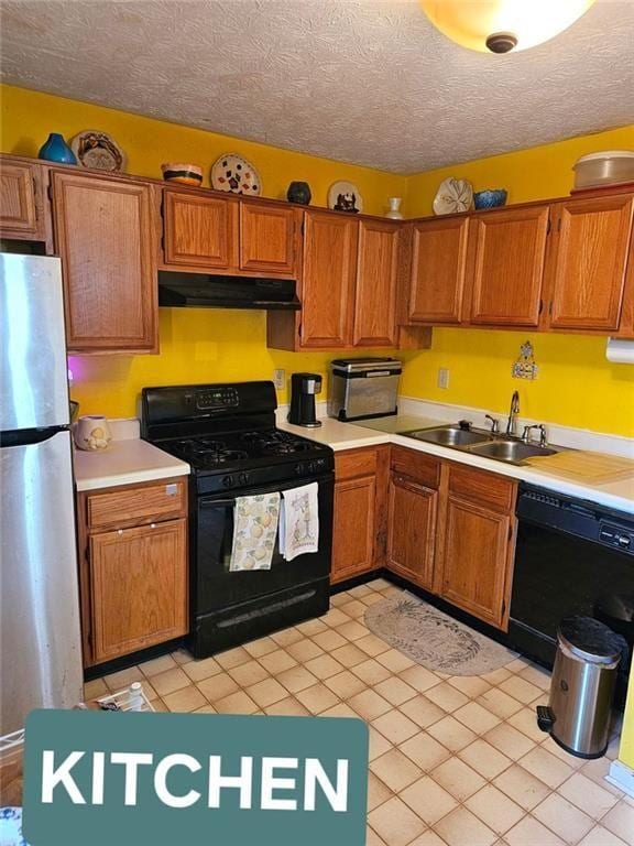 kitchen with light countertops, a sink, a textured ceiling, under cabinet range hood, and black appliances