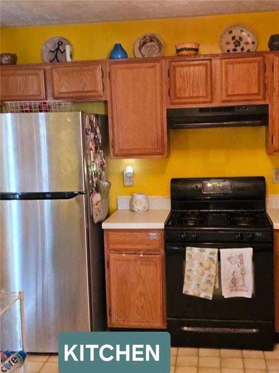 kitchen with brown cabinets, light countertops, freestanding refrigerator, gas stove, and under cabinet range hood