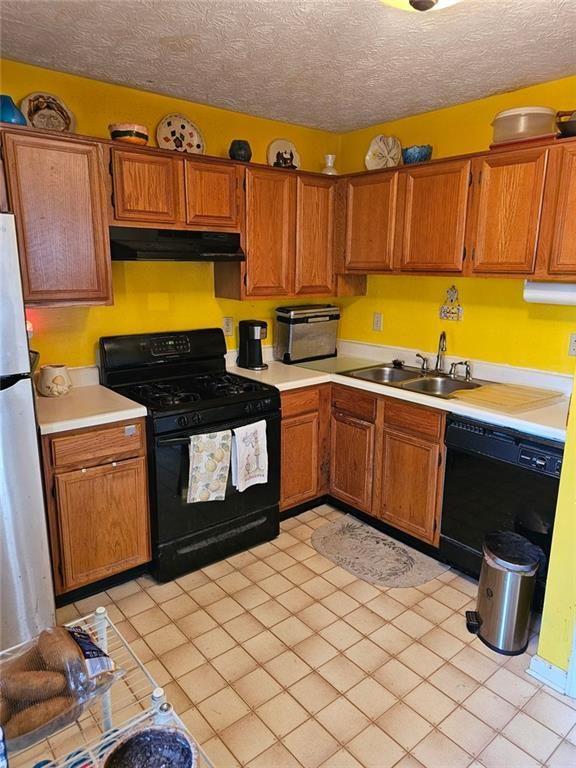 kitchen with brown cabinetry, under cabinet range hood, light countertops, black appliances, and a sink