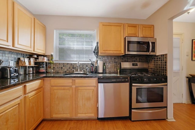 kitchen featuring sink, light hardwood / wood-style flooring, light brown cabinets, appliances with stainless steel finishes, and dark stone counters