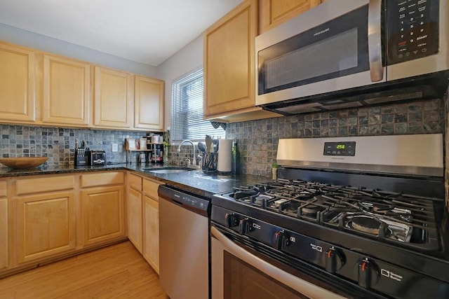 kitchen featuring stainless steel appliances, light brown cabinetry, sink, and dark stone counters